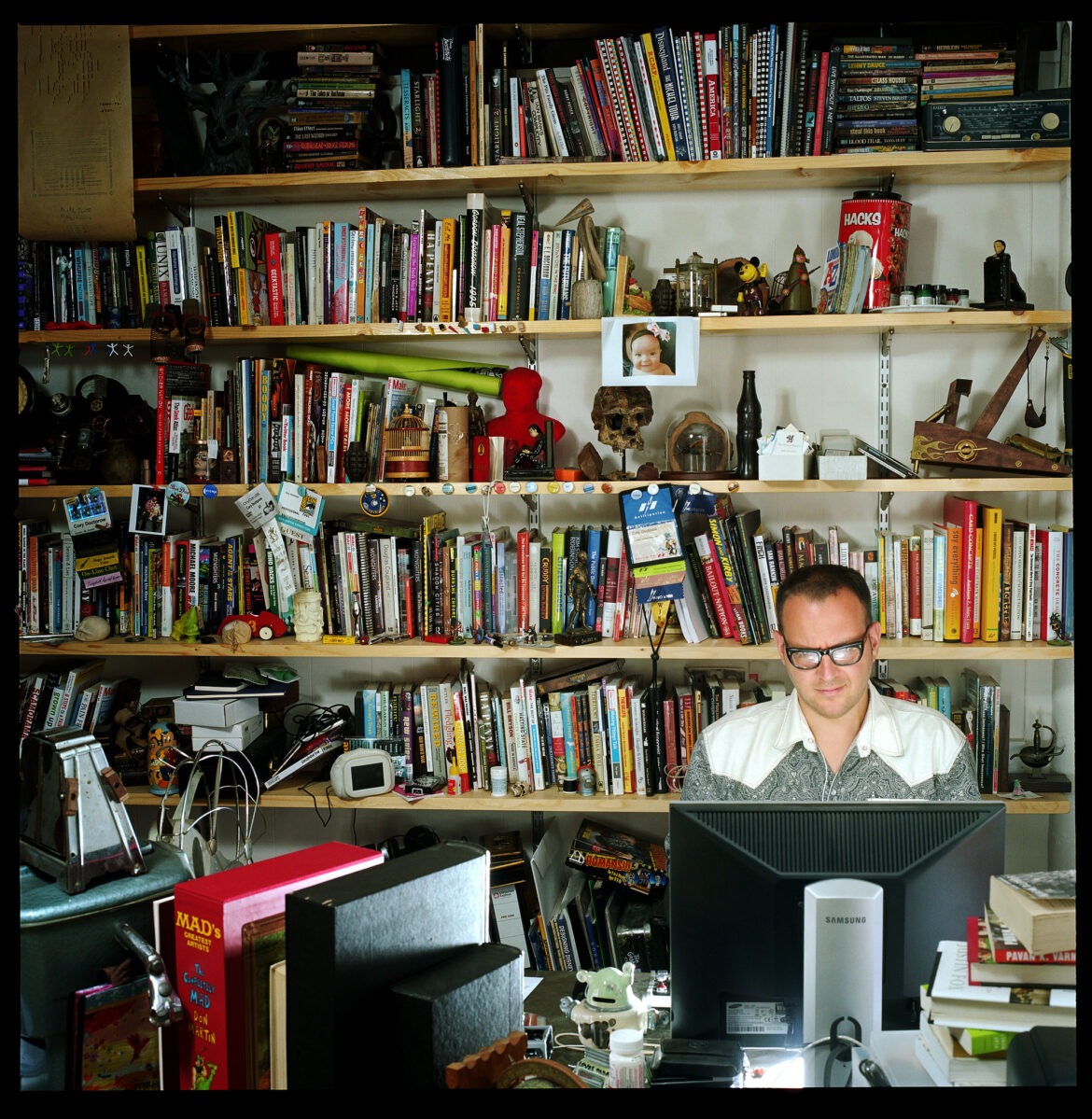 Photo of Cory Doctorow, working away at his desk. Portrait by Jonathan Worth